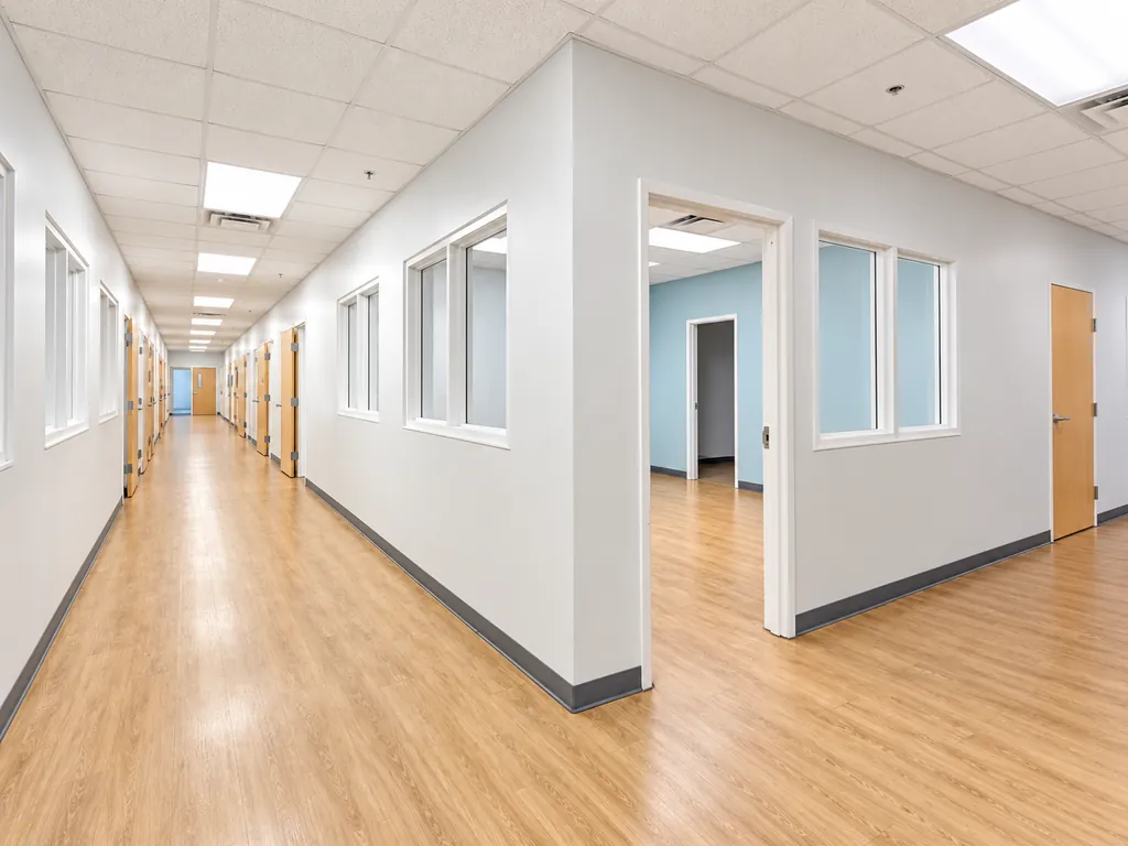 Existing condition: a corridor in the main building, with rooms on both sides behind interior windows and doors.