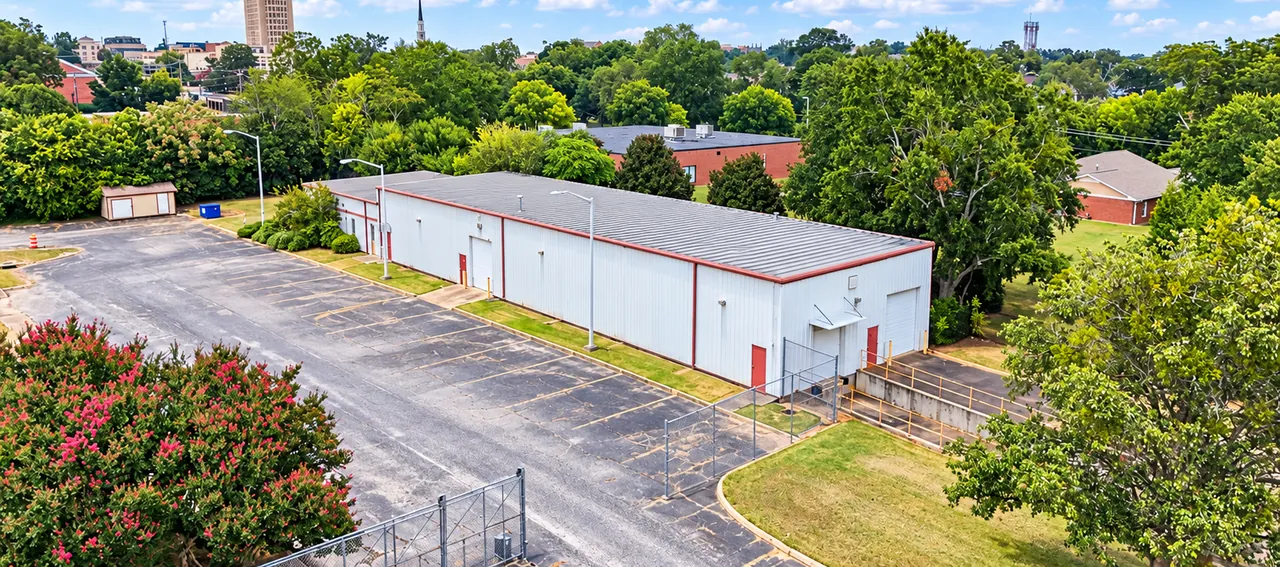 The long white metal second building with roll-up doors, a loading dock with a ramp, and the paved lot alongside.