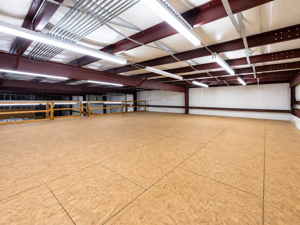 Existing condition: the open mezzanine in the metal building, with a bare board floor, exposed steel beams and strip lighting.