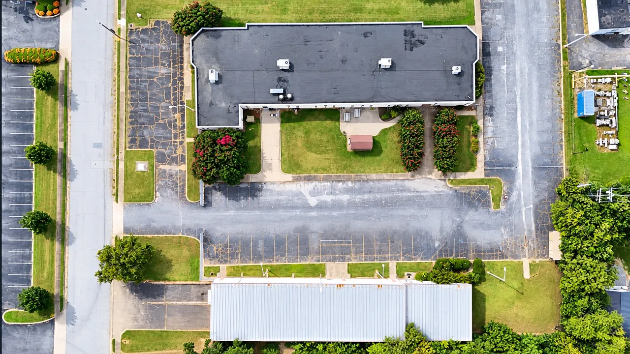 Overhead aerial view of the campus: the main building at the top, the paved parking area across the middle, and the long metal second building at the bottom, with South Church Street on the left.
